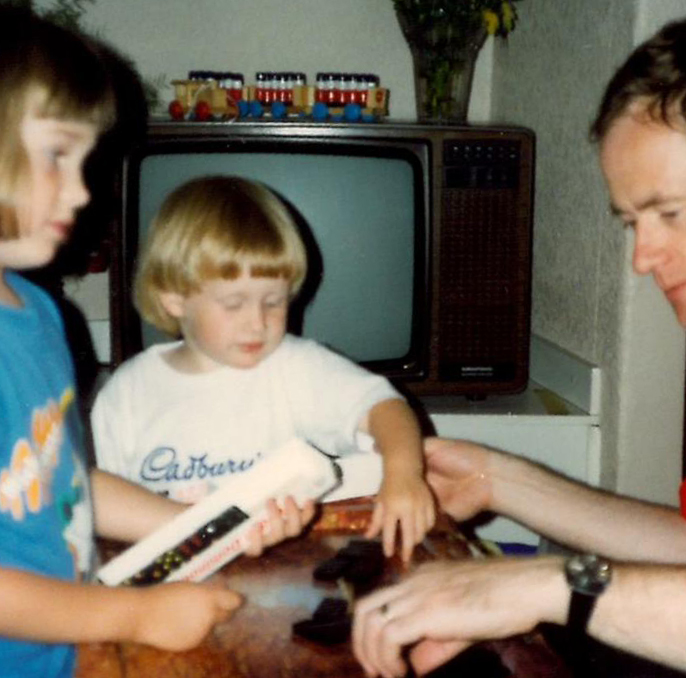 Old photo of children playing dominoes with dad, blonde one wearing cadburys tshirt