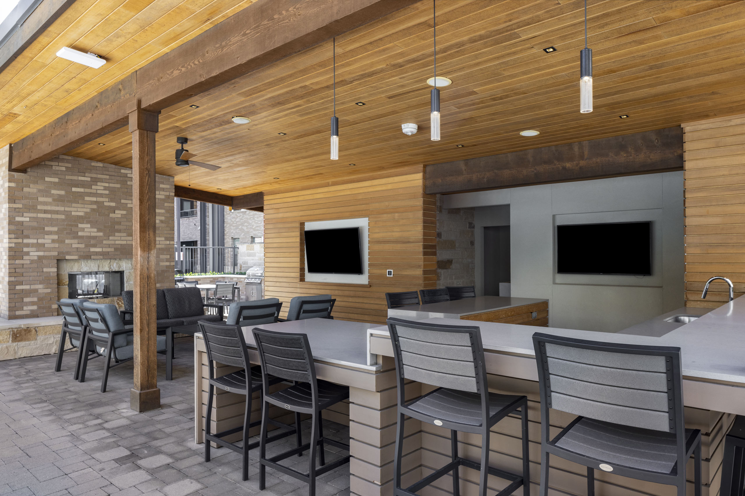 Daytime view of outdoor kitchen at AMLI on Aldrich with bar seating and large screen tvs and wood ceiling