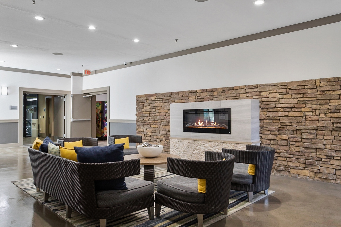 AMLI Old 4th Ward lounge area with fireplace on brick wall and brown woven seating with colorful pillows and coffee table