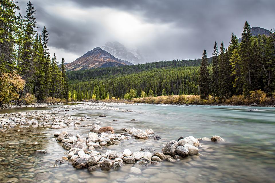 A clear river winding below a tall forested mountain on a cloudy day