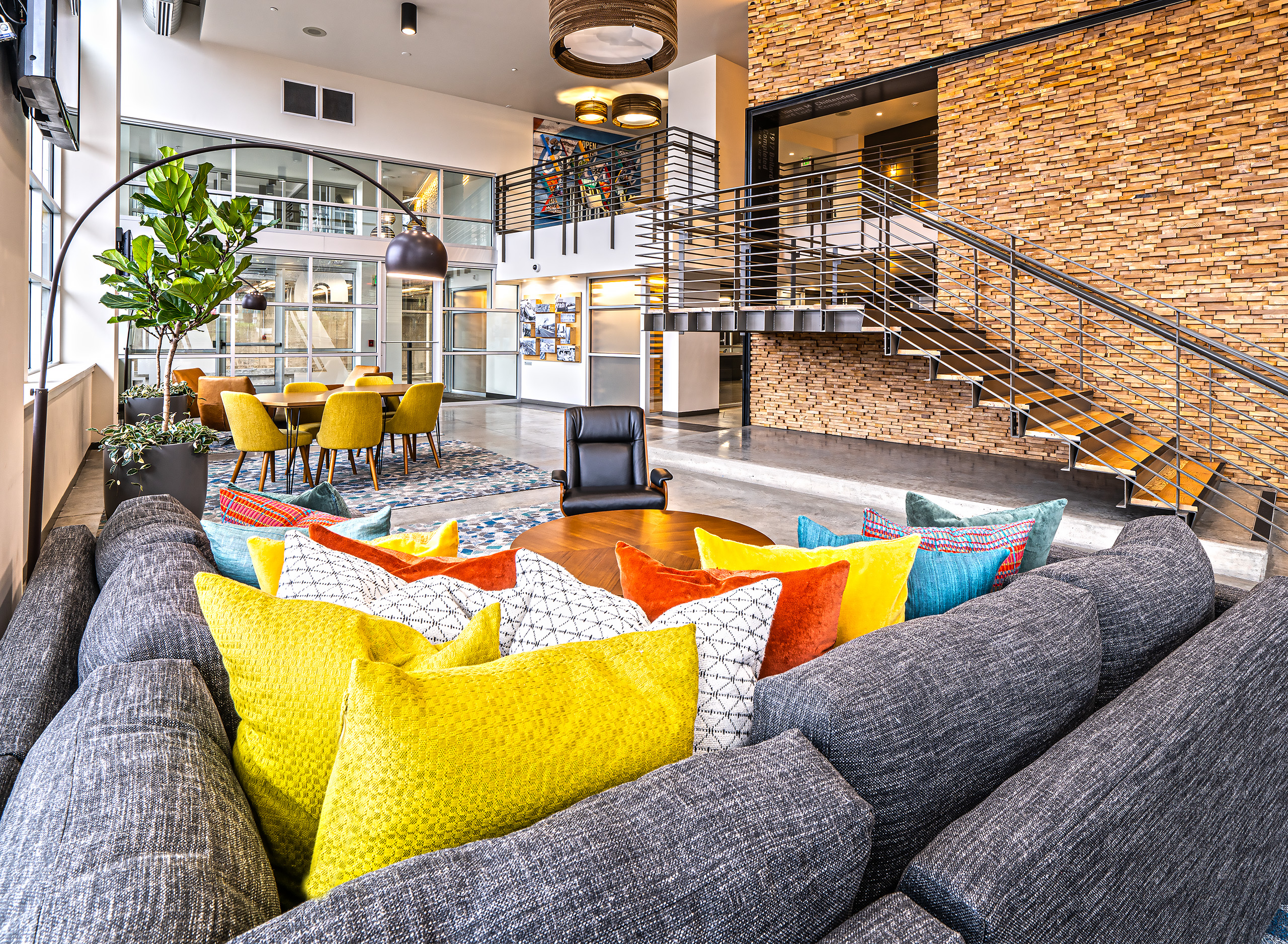 AMLI Mark24 two-story lobby with cozy seating areas and stone wall behind metal staircase and glass door and windows in rear