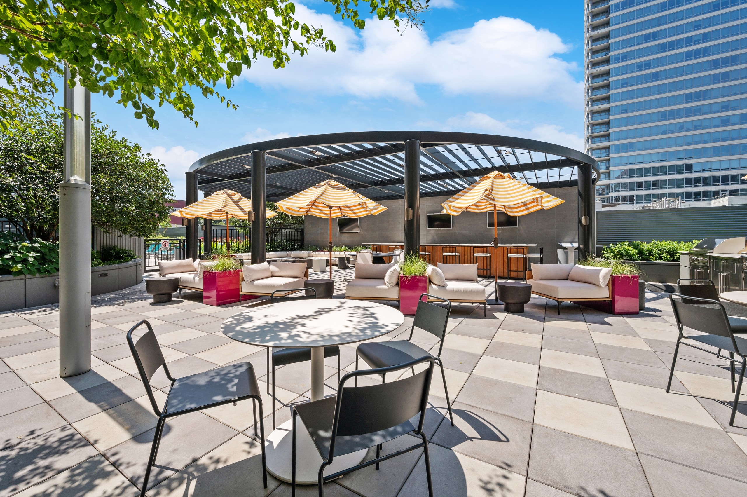 View of amenity deck lounge with dining tables and umbrella shaded patio furniture open to pergola covered bar at AMLI Lofts