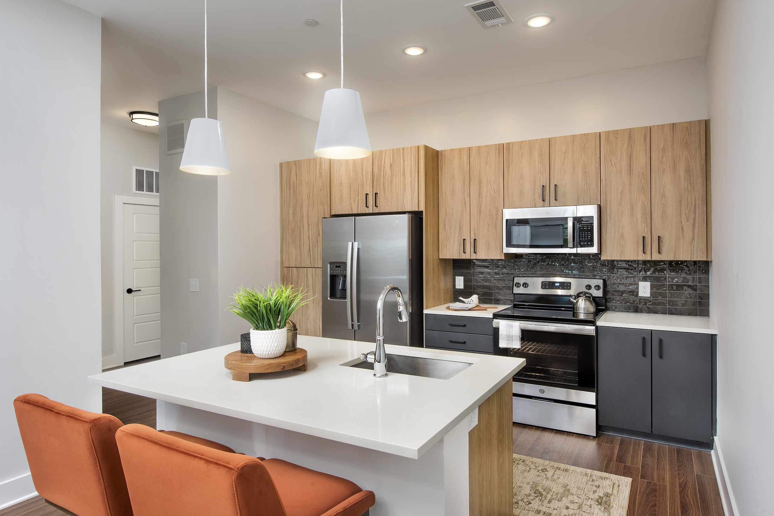 AMLI Flatiron kitchen with light woodgrain cabinets and stainless steel appliances with large white island and orange chairs