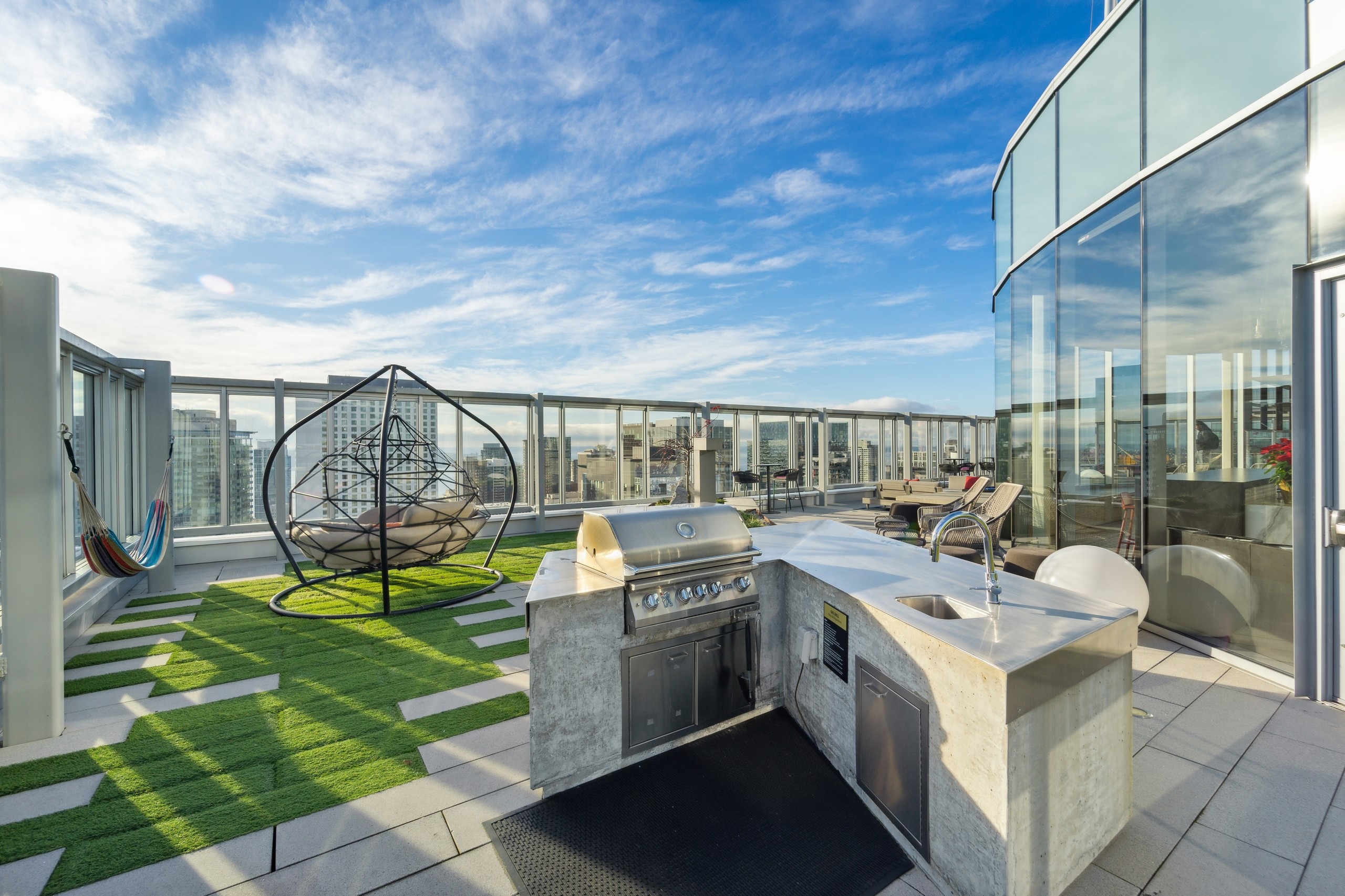 
Roof deck of AMLI Arc apartment building with a grill station and sink surrounded by a hammock and seating and city views