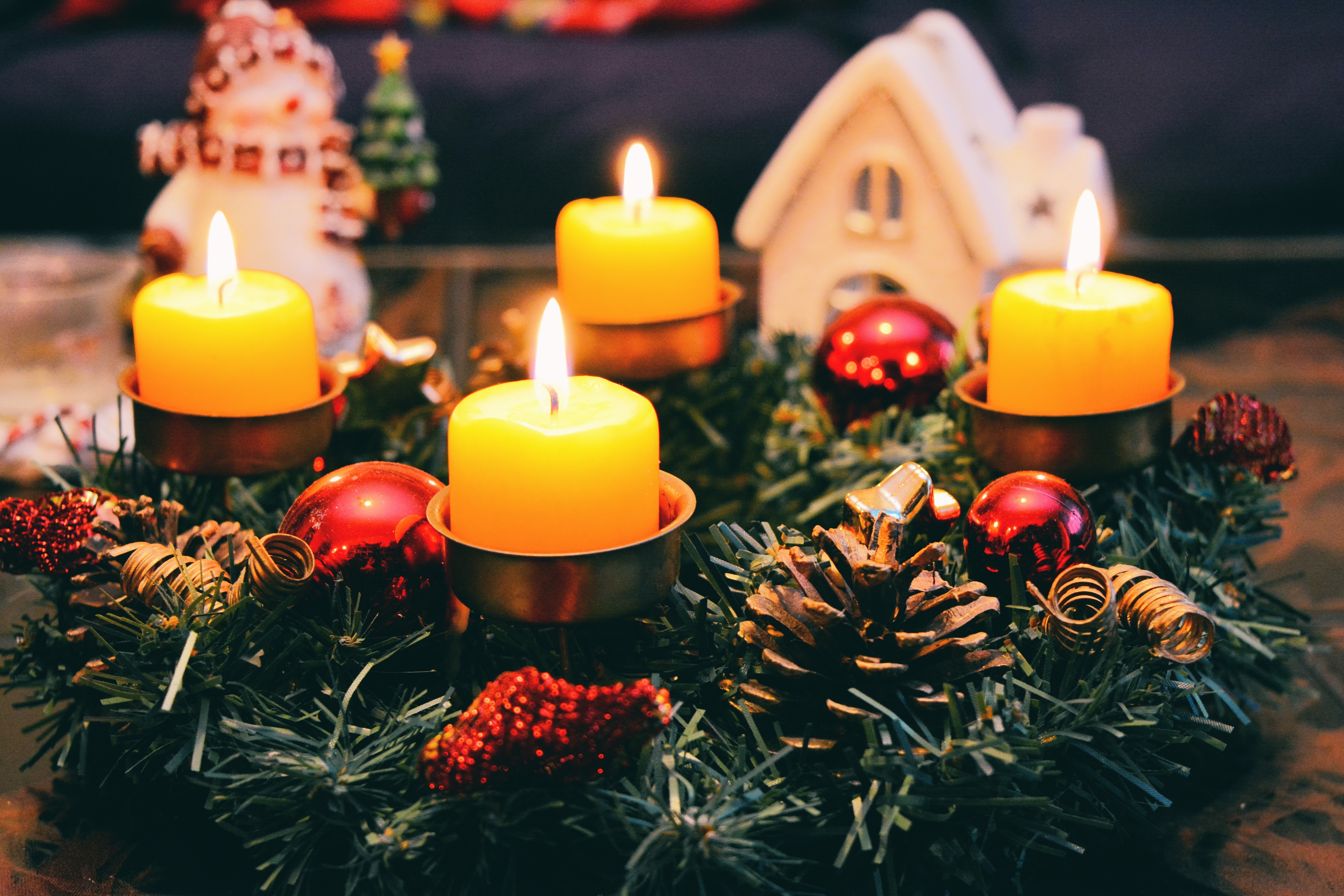 Four yellow advent candles in a green wreath on a table