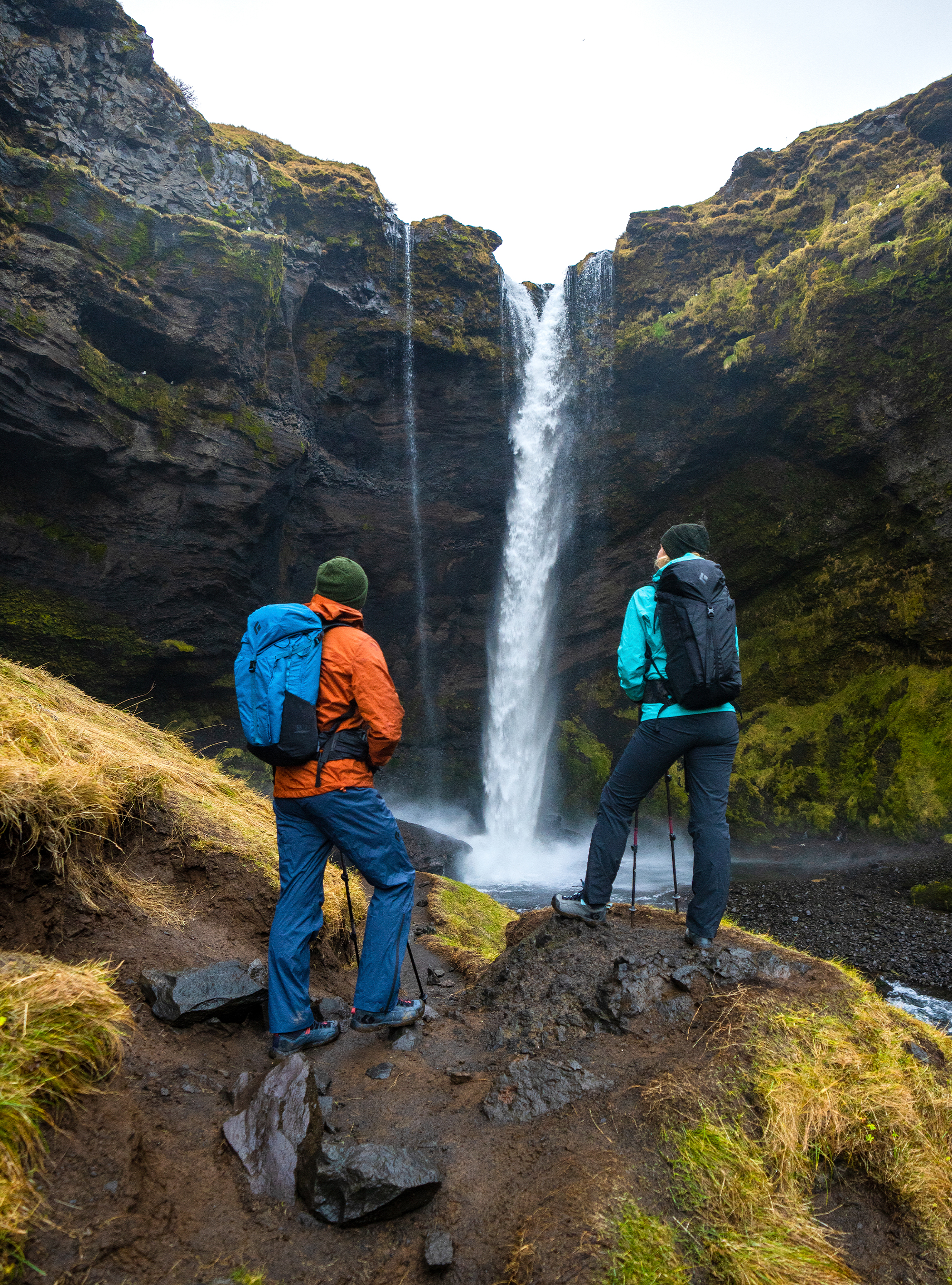 Two hikers wearing Black Diamond technical rain shells in front of a waterfall on a cold drizzly day.