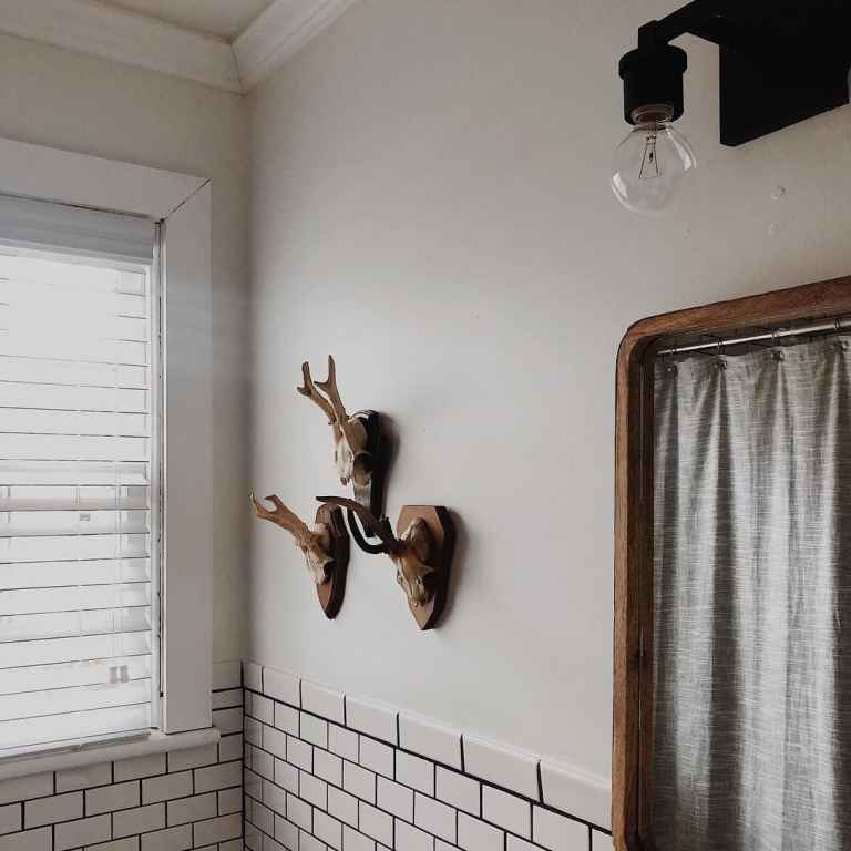 vintage inspired bathroom with antique mirror, mounted animal horns, subway tile and white faux wood blinds covering window