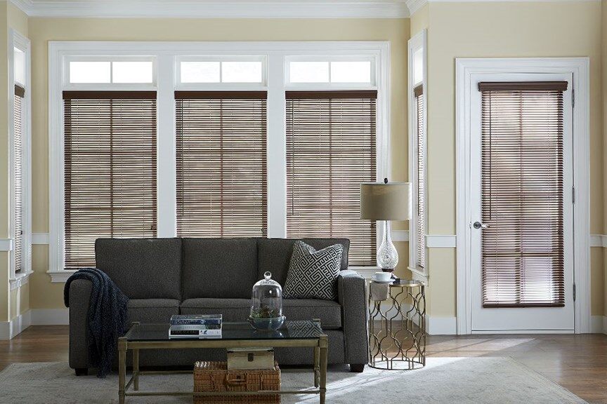 contemporary living room with grey couch, yellow walls and medium to dark brown 1 faux wood blinds in the windows and over the door.