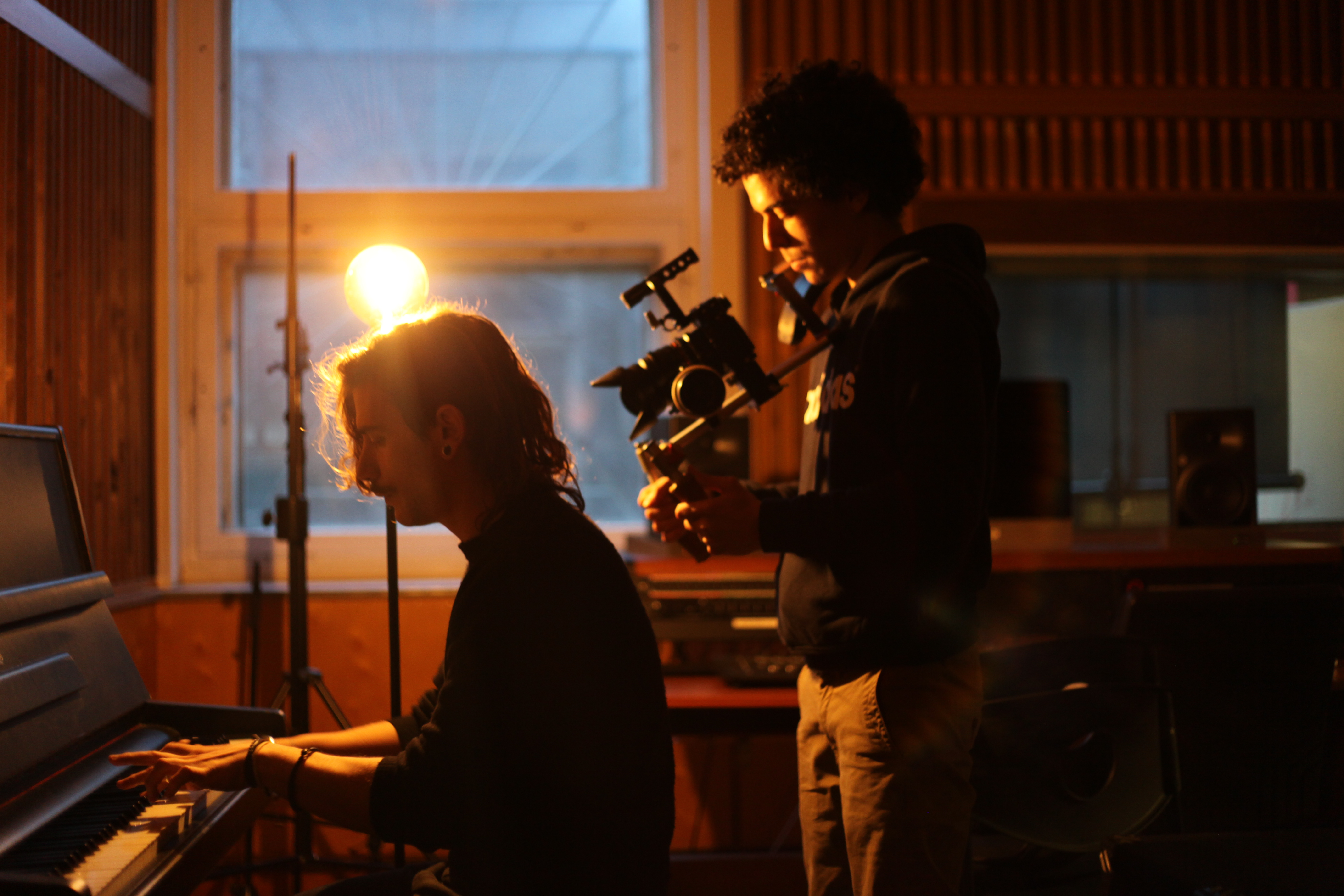 a student performs on the piano in the studio while another records them