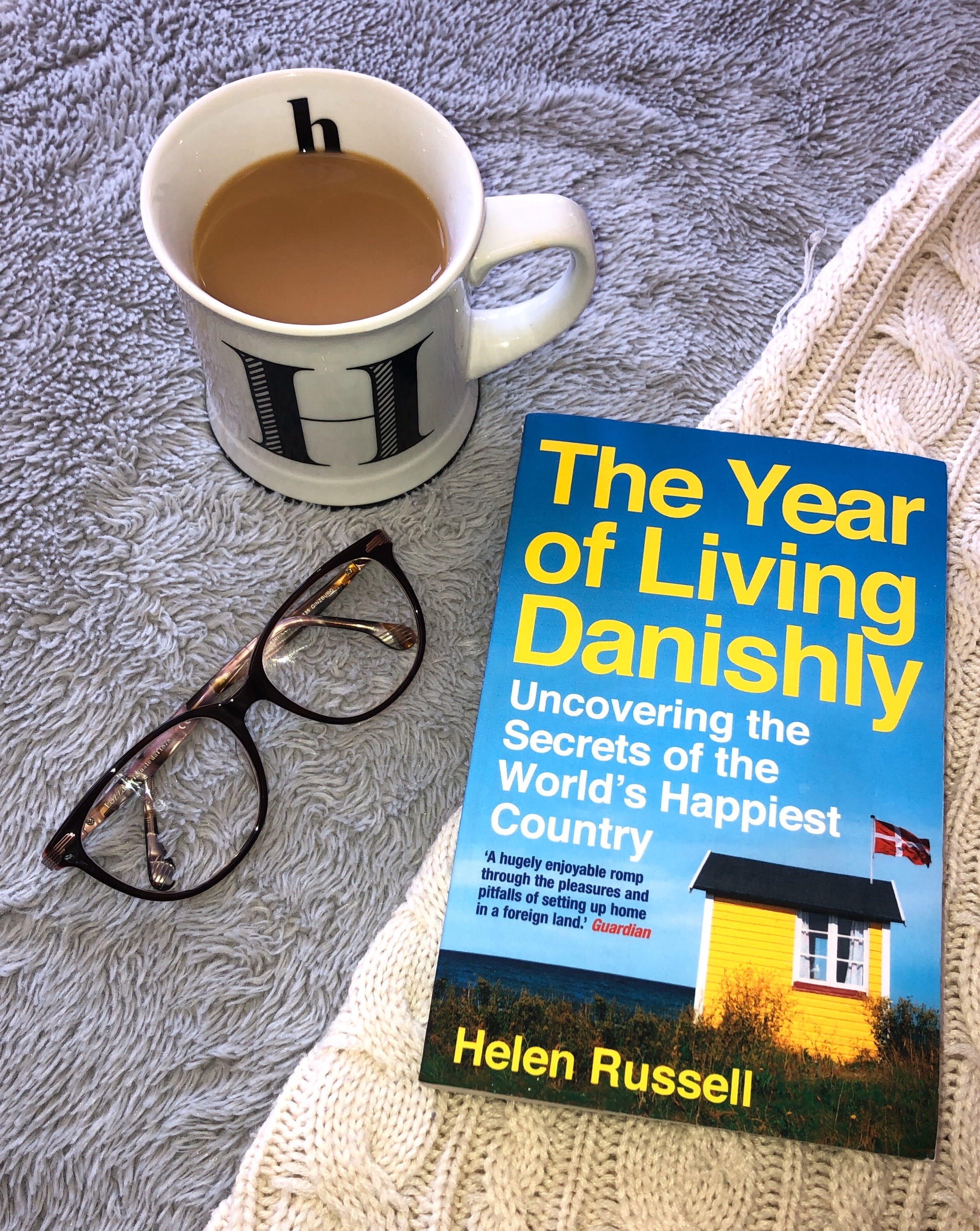 A book titled 'The Year Of Living Danishly', next to a pair of glasses and a cup of tea