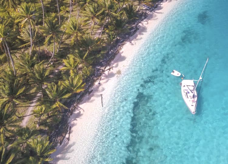 Panama San Blas Adası'nda çekilen fotoğrafta; beyaz kum, ormanlık alan ve okyanus üzerinde duran bir tekne bulunuyor.