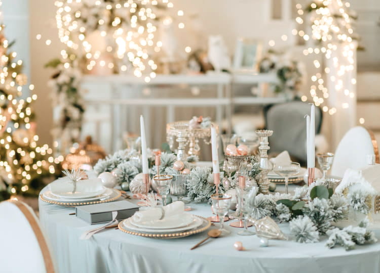 Kış düğünü konsepti ile hazırlanmış ve ışıklandırılmış olan düğün salonu içerisinde yemek masası bulunuyor. Yemek masasında tabaklar, mumlar, kaşıklar ve kış temasını yansıtan süslemeler duruyor.