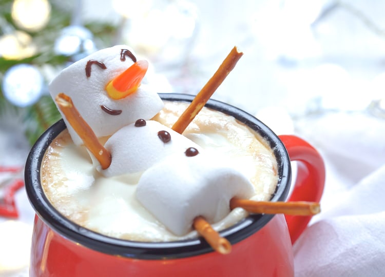 Kırmızı geniş ağızlı bir bardak içerisinde kahve ve üzerinde marshmallowlar birleştirilerek kardan adam şekli verilmiş yenilebilir bir süs bulunuyor.