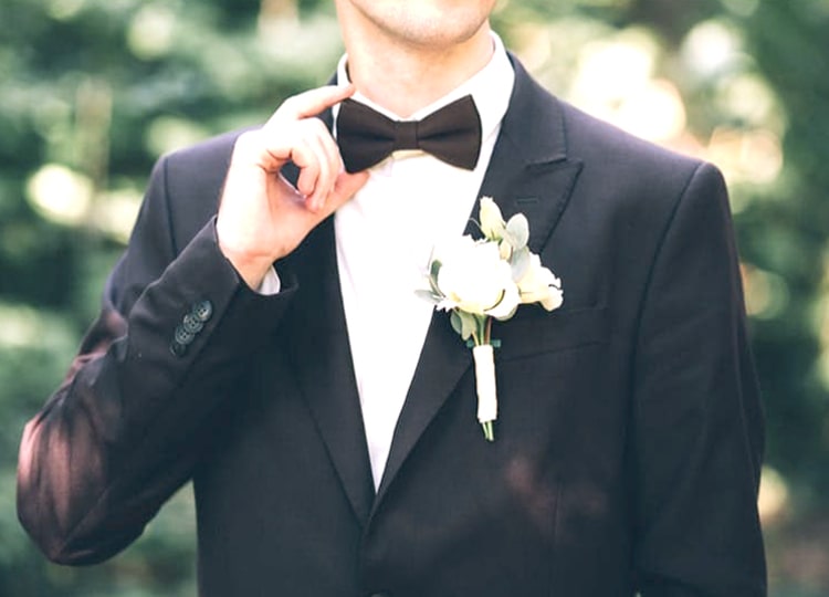 Yakın plan çekimde yeşillik bir arka plan önünde duran damat; sağ eli ile papyonunu tutuyor. Damadın sol cebinde küçük bir çiçek demeti bulunuyor.