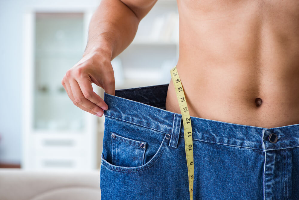 Man is checking his jeans showing his weight loss progress