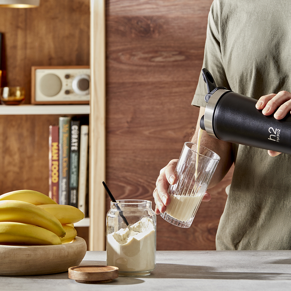 man standing by kitchen counter pouring smoothie into glass from protein shaker. father's day gift guide. The Sports Dad.