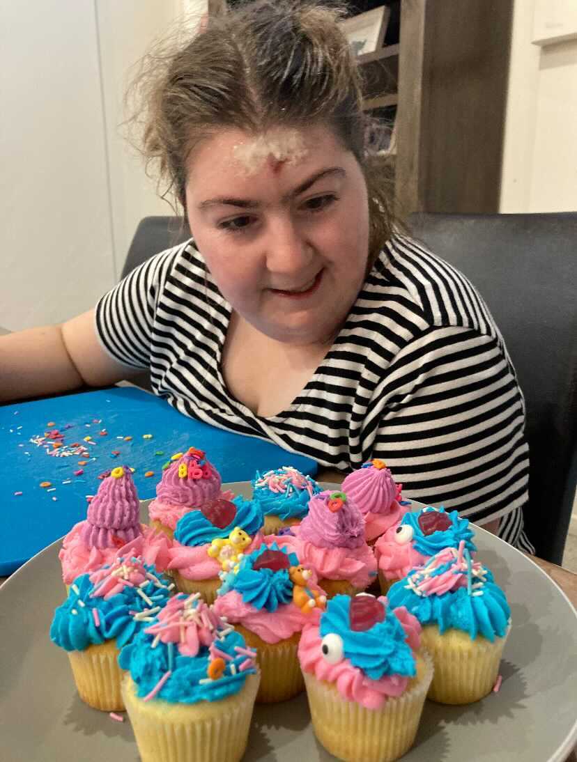 Ella looks at 10 colourful cupcakes. She's sitting down and wears a striped t shirt.