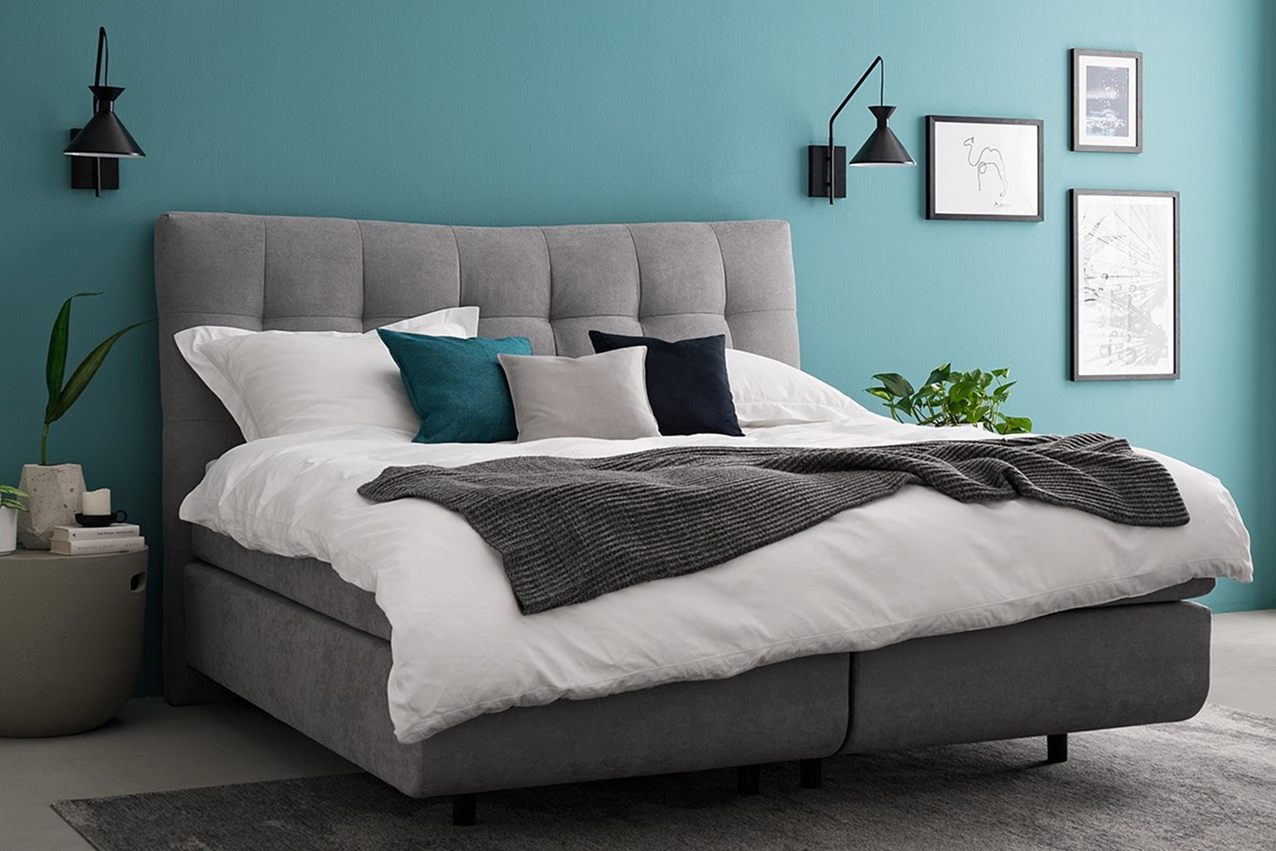 Graues Bett in Schlafzimmer mit türkiser Wand und schwarzen Wandleuchten