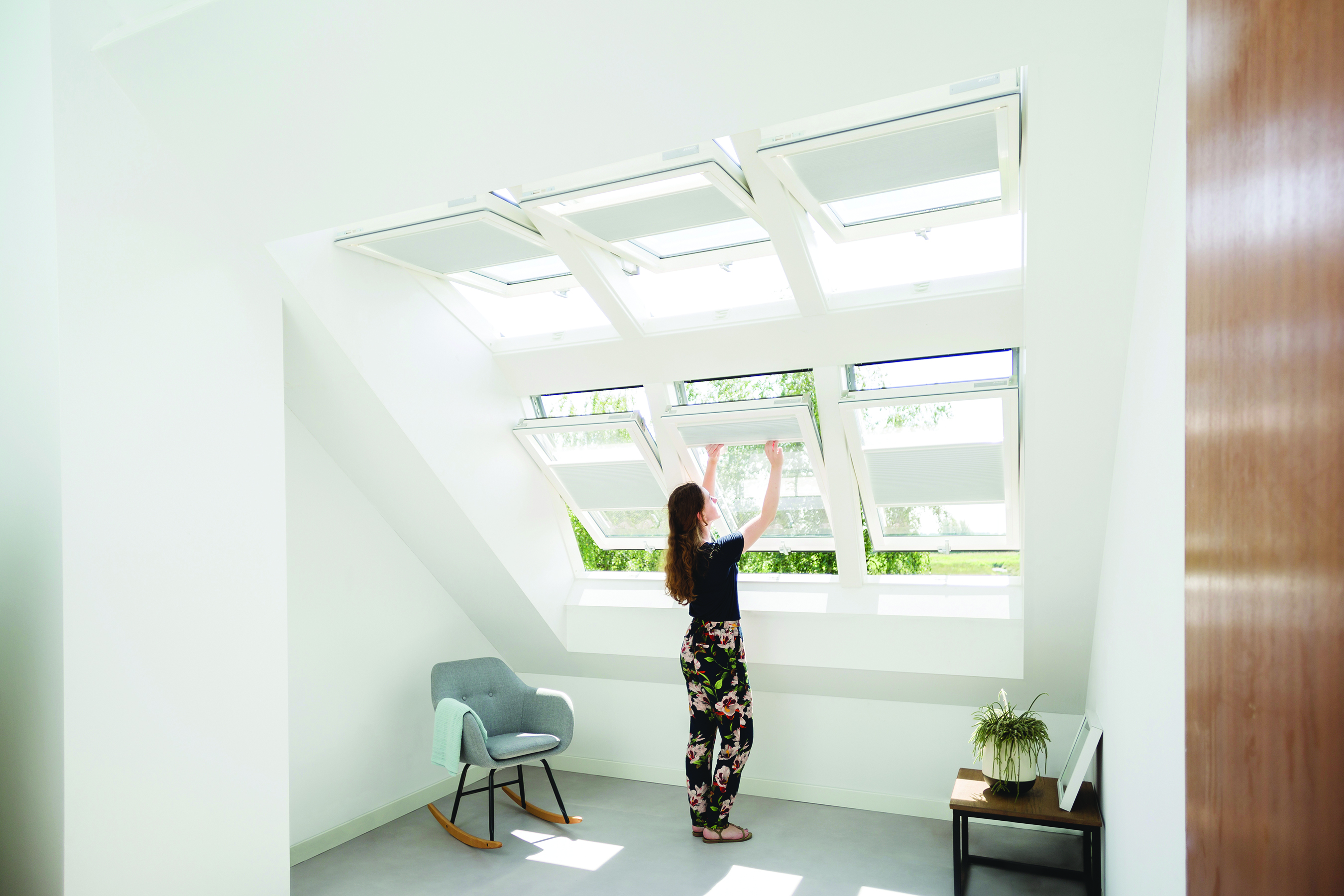 Frau öffnet das mittlere von sechs Dachfenstern in einem hellen modernen Raum