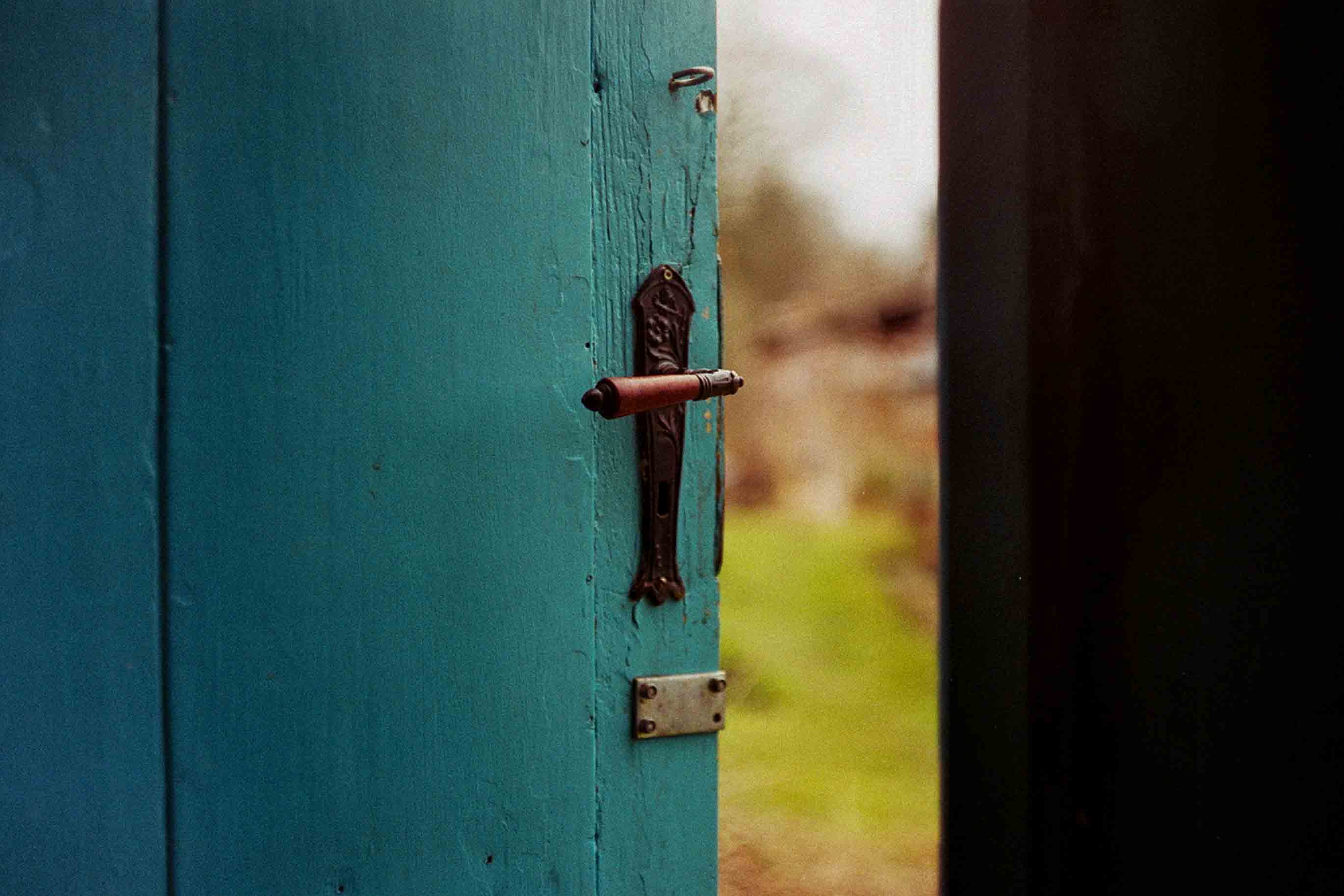A turquoise door slightly ajar, showing a green, lush field outside. 