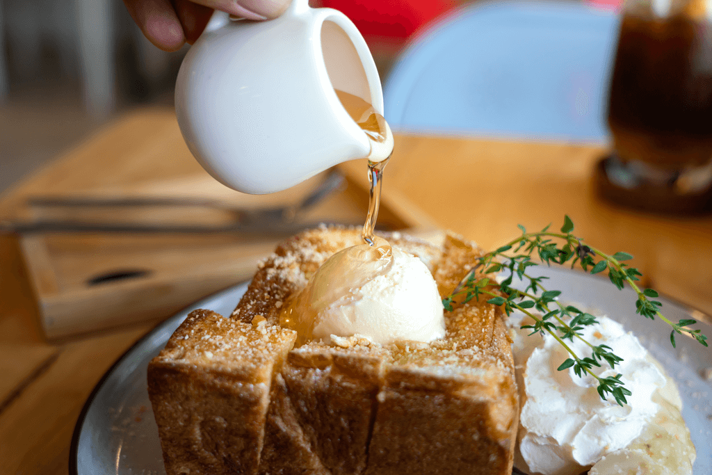 A woman's hand pours honey over Japanese thick toast with ice cream on top in a Shibuya cafe.