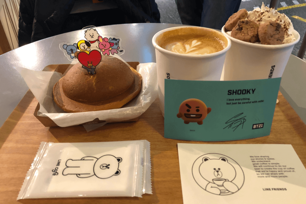 A tray of BT21 sweets, a cup of coffee, and a cup of ice cream topped with cookies with Line Friends wet wipes and a card on the tray.