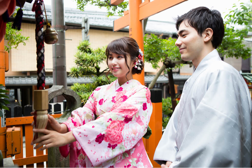 A couple wearing kimonos ring a bell at a shrine during the first prayer of the new year