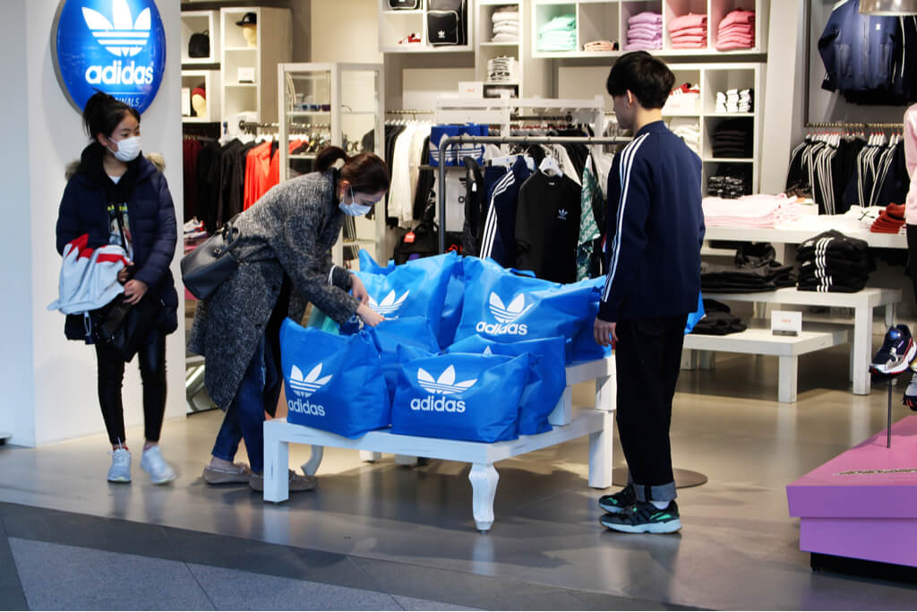 Two women choose a lucky bag from Adidas as a shop staff helps the women