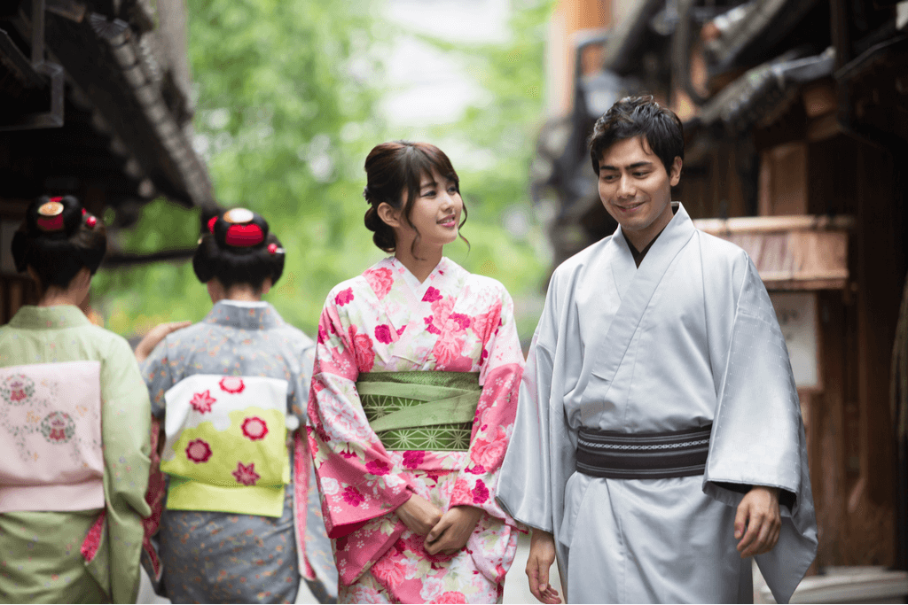 A Japanese couple walk down an old-style street in Kyoto Japan wearing a yukatas as they walk past two women in yukata too, enjoying the traditional Japanese vacation vibes