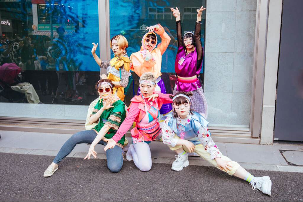6 young women pose in bright, colorful clothing on the street.