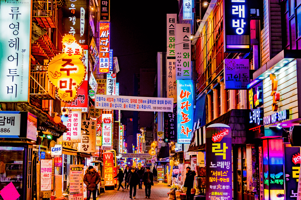 The streets of Seoul lit up with many neon lights as people walk down the streets checking out the different stores and restaurants.
