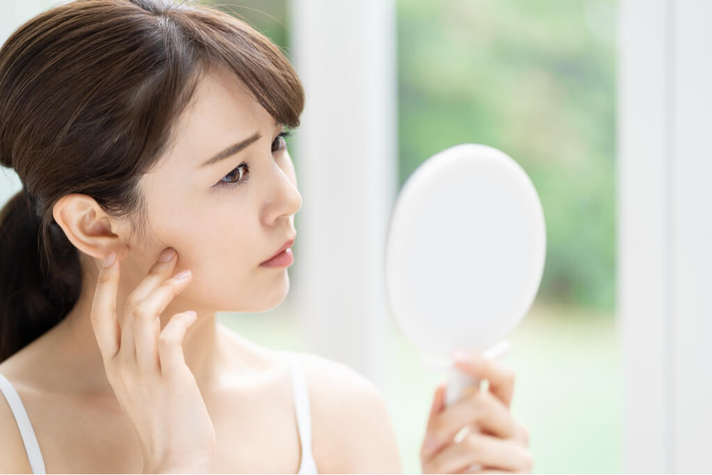 A woman checking her skin in a mirror looking worried 