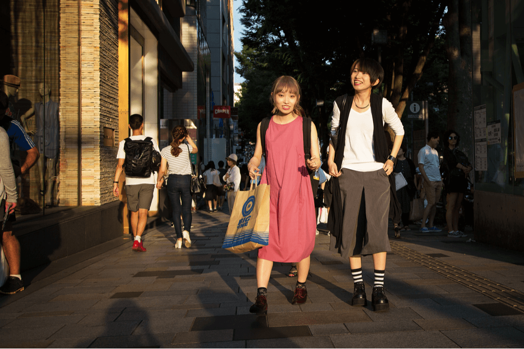 Two women walking down the street in Harajuku with one holding a shopping bag as they both smile