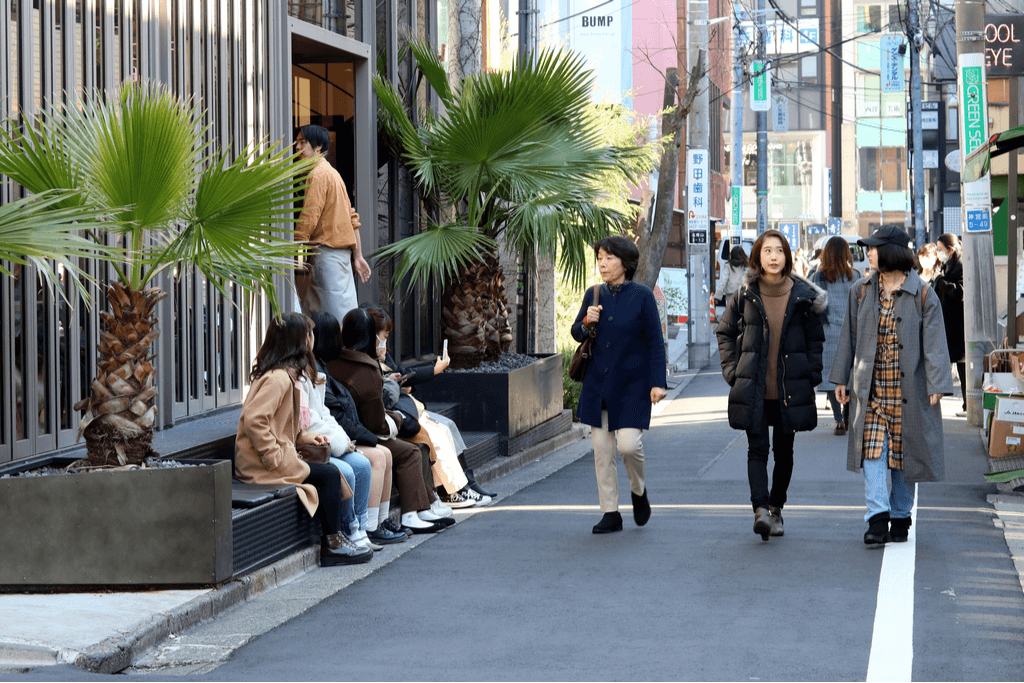 Women walk down a street of the fashion district Omote-Sando, with teen girls sitting in front of a store waiting to enter.