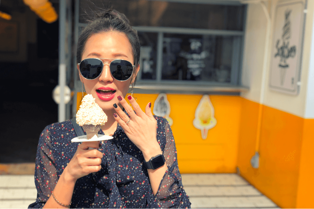 A young Korean woman wearing sunglasses and makeup enjoys a sweet ice cream treat in Seoul at an ice cream stand.