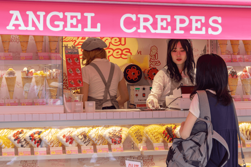 A woman purchasing a crepe at a crepe stand called Angel Crepes in Harajuku with two staff members in it.