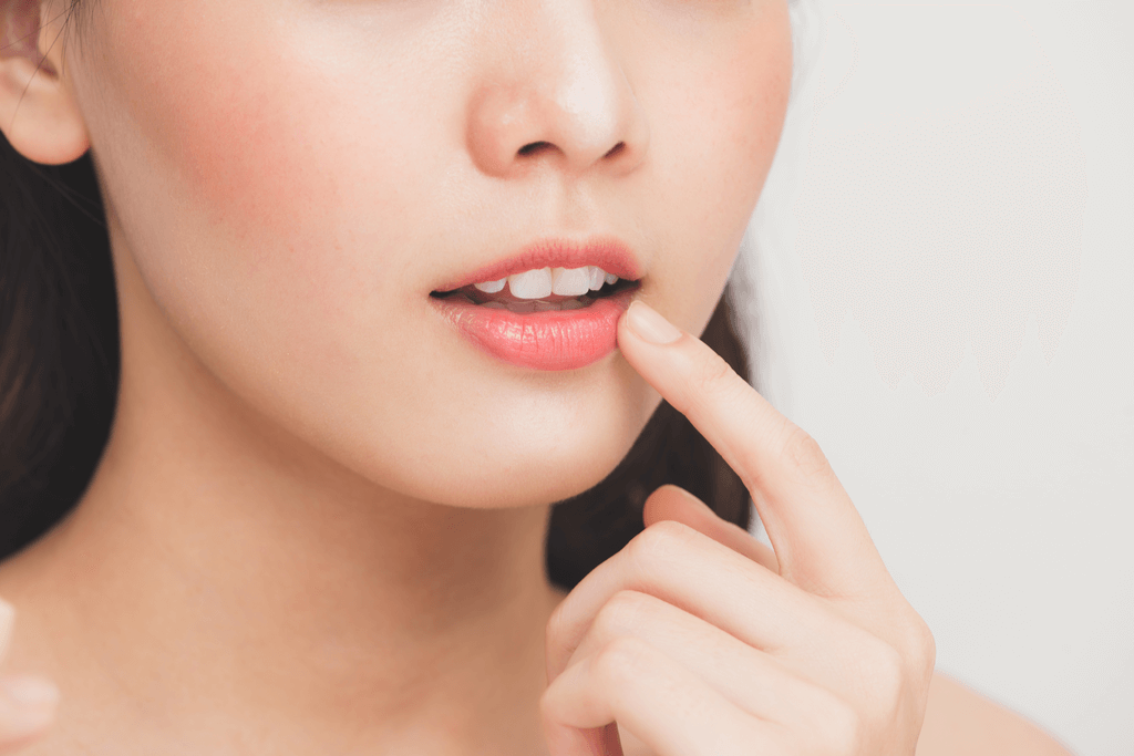 A young woman touches her lips to show how soft and plump they are in front of a white background.