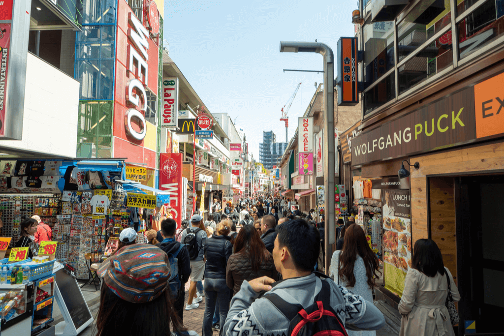 Many people walking down the Takeshita Street with many restaurants and store signs in the background.