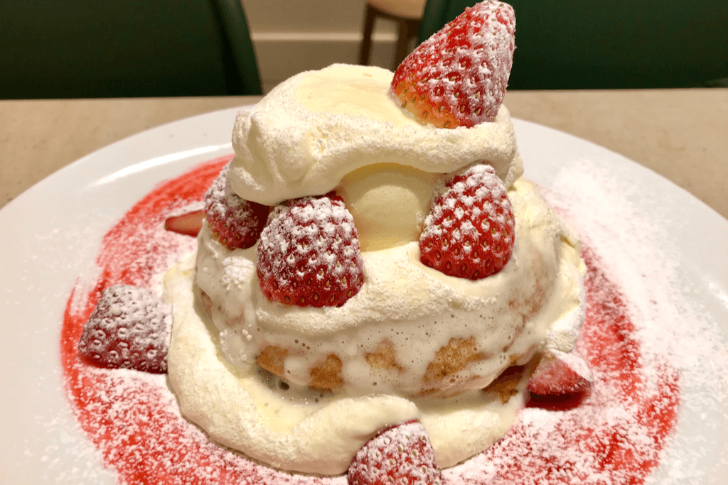 Two fluffy pancakes topped with whipped cream, strawberries, and a scoop of vanilla ice cream on a plate red and white plate in a Tokyo cafe.