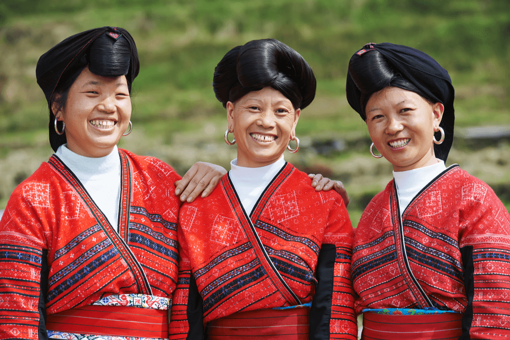 Three Yao women, inspiration for many Korean hair care products, with their long hair tied into elaborate styles, smile as they stand in their traditional garb.