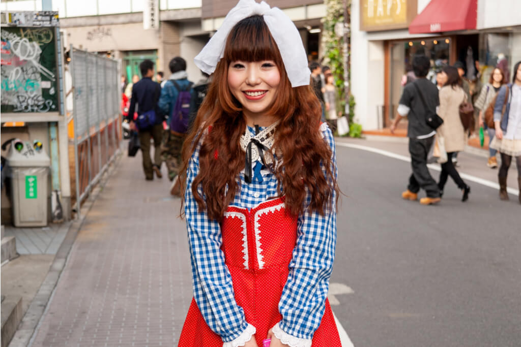 A girl in a red an blue shirt and dress stand on the streets of Tokyo for a photo
