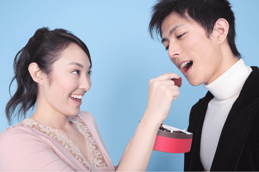 A woman feeds a man some chocolates from a Japanese Valentines gift box that she gave him