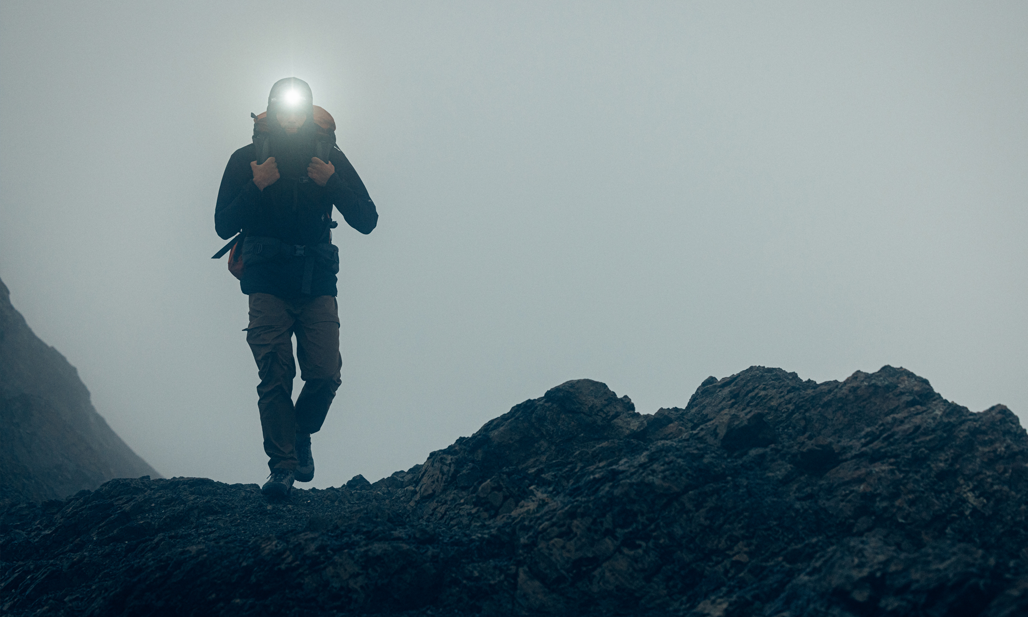 Backpacker with a headlamp in foggy conditions on rocky terrain.