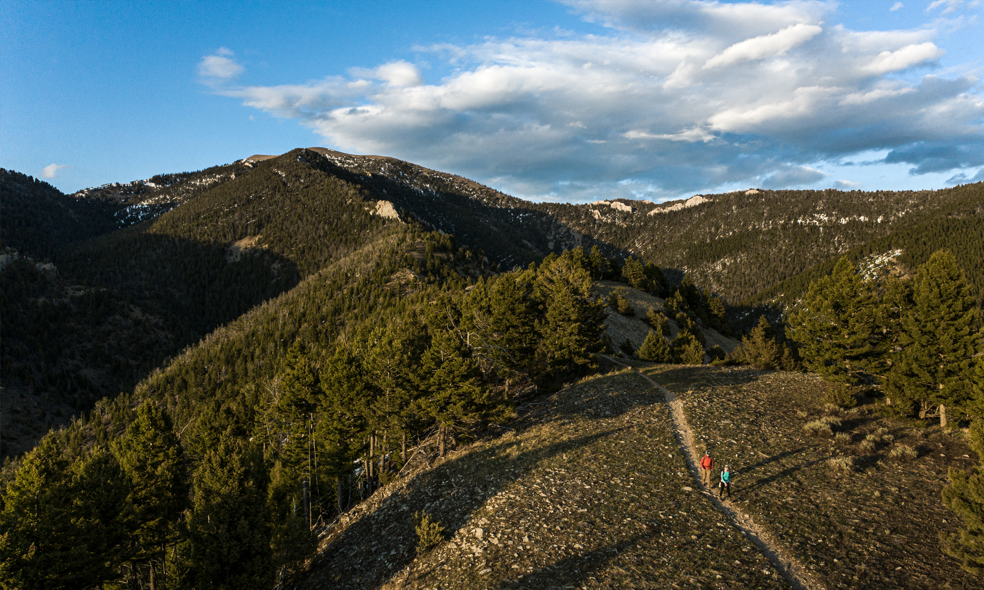 Aerial view of two people hiking on a trail in the mountains.