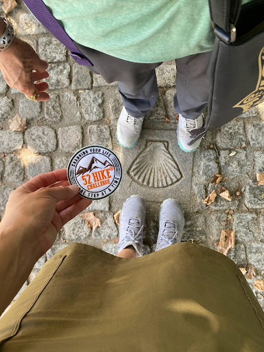 Two people standing on the Camino de Santiago wearing Oboz Katabatic hiking shoes and holding a 52 Hike challenge sticker. 