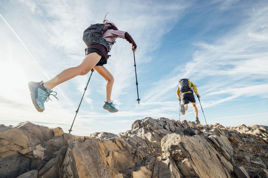 Two runners in Oboz Katabatic trail shoes leap across rocky terrain 