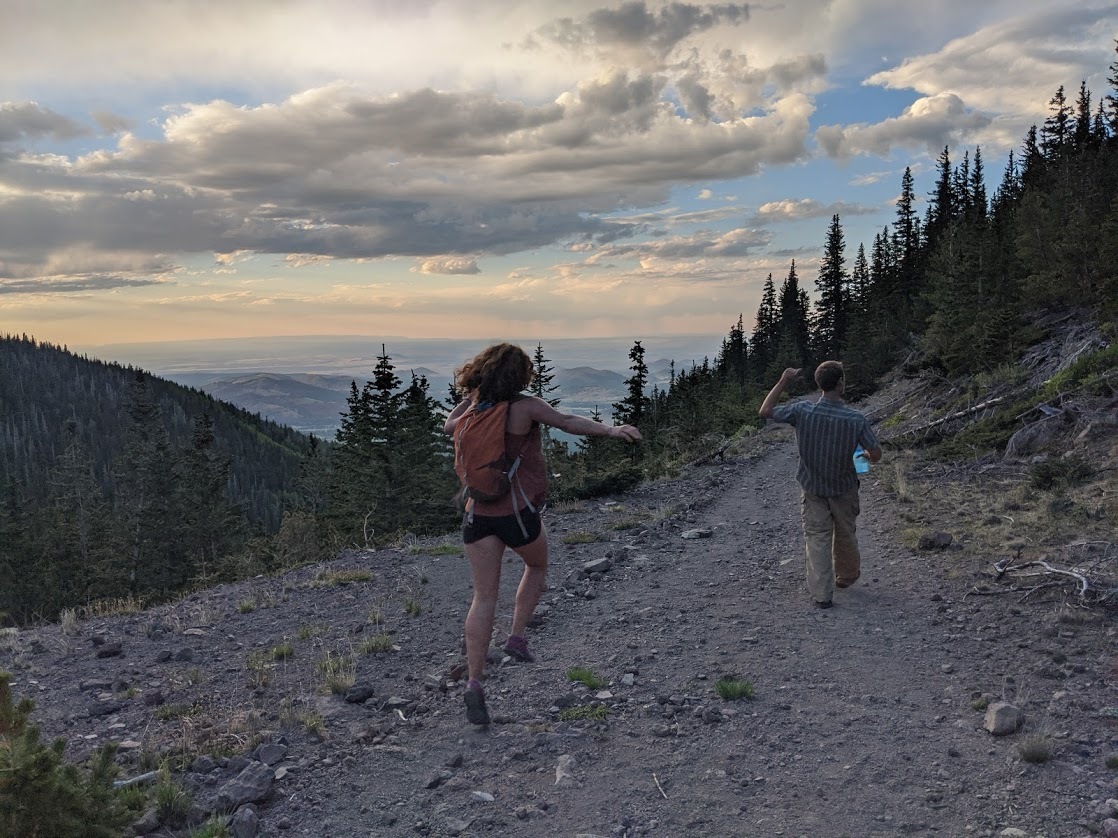 Two hikers skipping on trail as the sun sets 