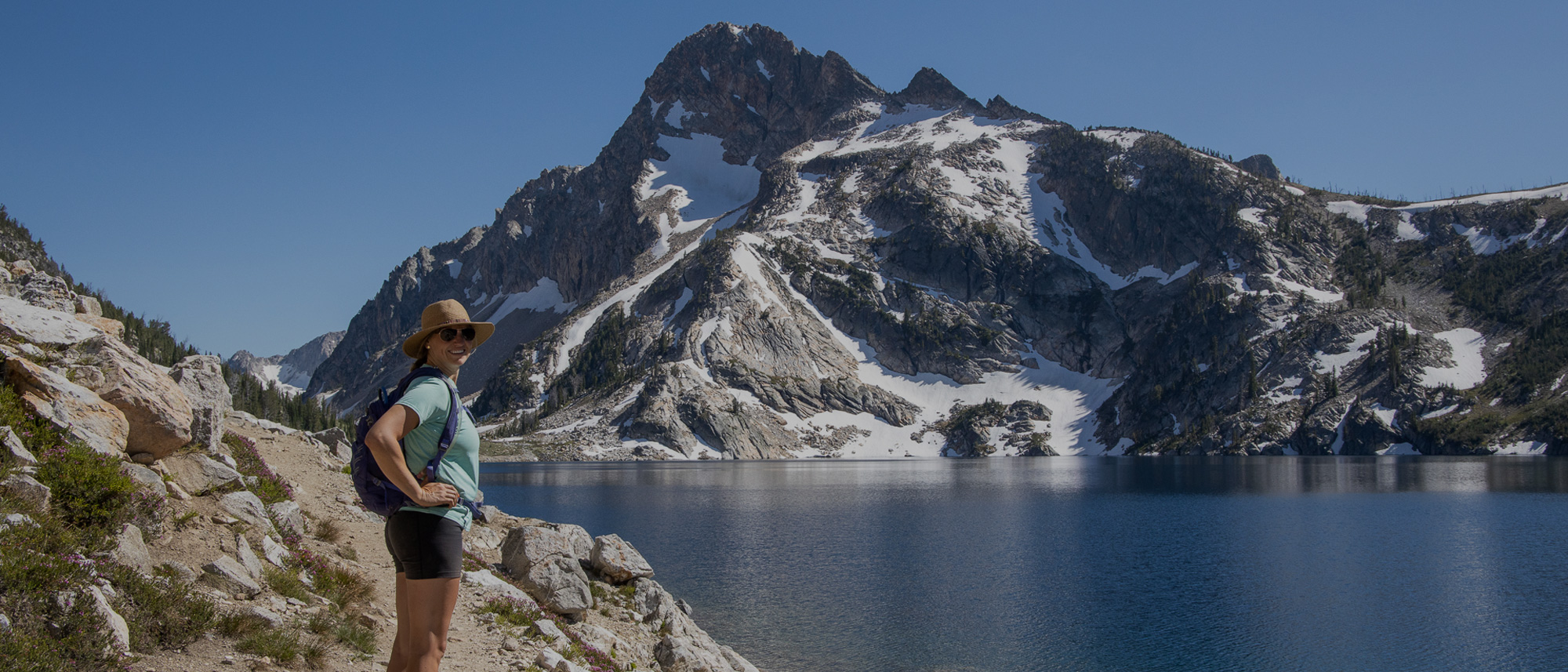 Hiker posed in front an alpine lake and snowy mountain wearing Oboz hiking shoes