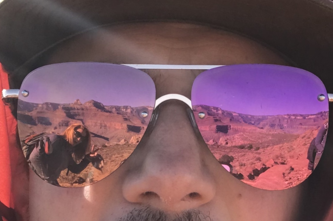 The reflection of glasses showing a hiker and layers of a canyon