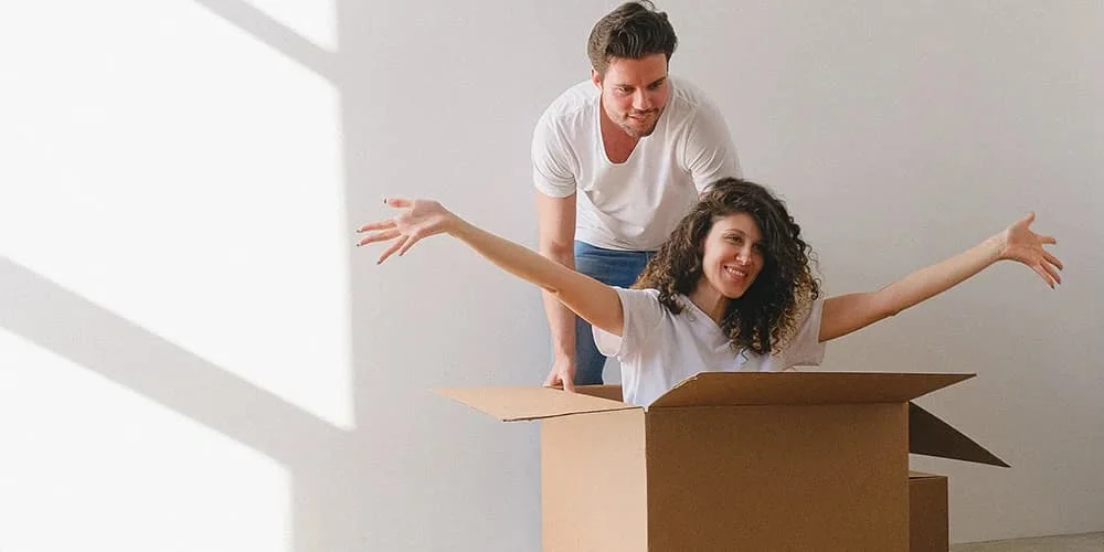 büyük kutunun içinde oturan bir kadın ve arkasında duran bir adam